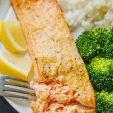 A fork flakes the end of an air fryer salmon fillet on a white plate served with broccoli and rice.