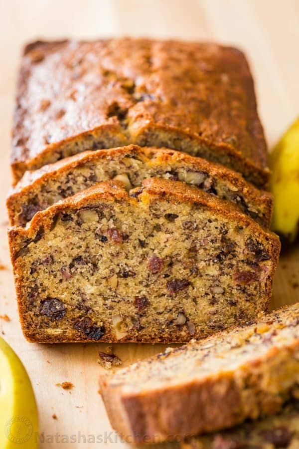 Banana Bread on a cutting board with walnuts, raisins and ripe bananas to make healthy banana bread