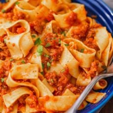 Pappardelle pasta with bolognese sauce in a blue bowl, with a fork.