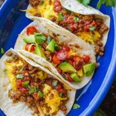 Overhead view of three breakfast tacos with chorizo on a blue oval plate.