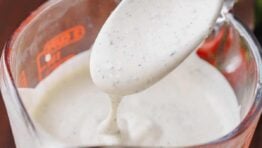 A spoon drizzles ranch dressing into a measuring cup.