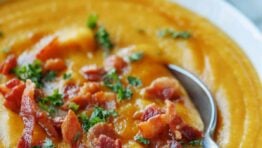 A bowl of homemade butternut squash soup garnished with bacon and parsley, with a spoon.