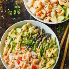 Overhead view of two California roll bowls topped with a drizzle of spicy mayo next to chopsticks.