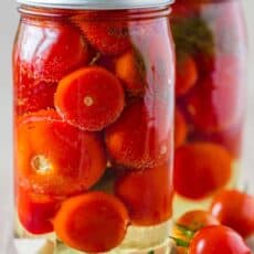 Two jars of canned tomatoes next to fresh tomatoes on the table