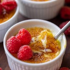 Creme brulee topped with raspberries, with the caramelized sugar topping cracked with a spoon.