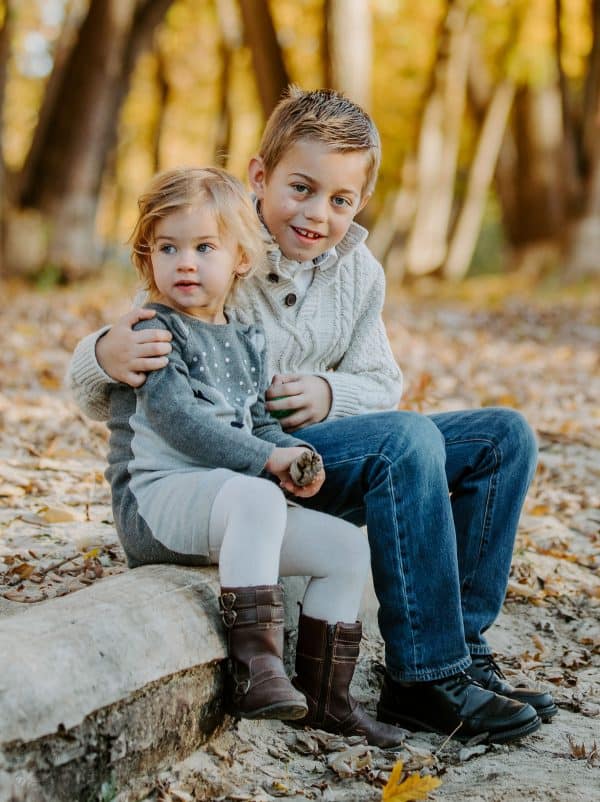 Siblings sitting on a tree log hugging 