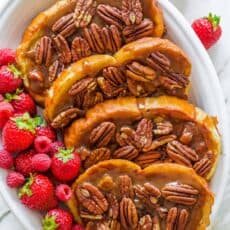 Slices of caramel french toast arranged on a platter with berries scattered