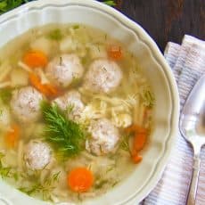 A bowl of mom's meatball soup with a cloth napkin and spoon beside it