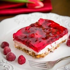 A slice of raspberry pretzel jello on a plate with raspberries beside it