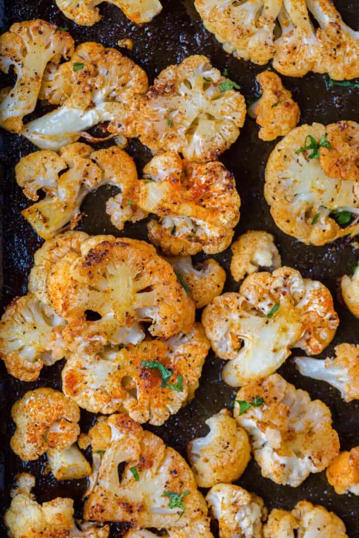 Roasted caulilfower florets on a baking sheet topped with fresh chopped greens. 