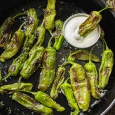 Shishito peppers in cast iron skillet with bowl of dipping sauce