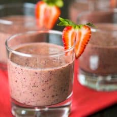 A glass of strawberry spinach smoothie garnished with a strawberry with more glasses in the background