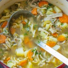 Hearty turkey noodle soup being scooped out of a pot with a large ladle