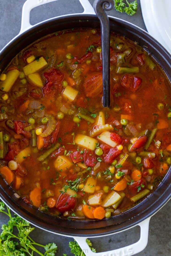 a pot of vegetable soup with herbs next to it